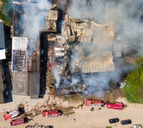 Aerial view of firefighters extinguishing ruined building on fire with collapsed roof and rising dark smoke.