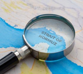 Magnifying glass focusing on the Strait of Hormuz on a map. Geopolitics, global trade, oil shipping routes concept.