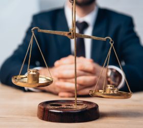 selective focus of golden scales near lawyer with clenched hands